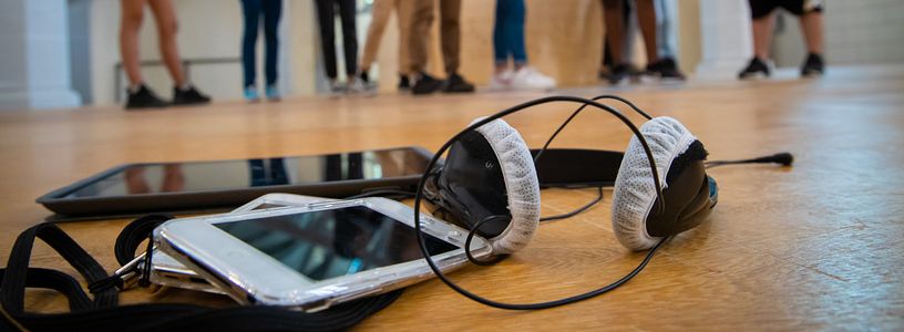 Audioguide-Gerät mit Kopfhörer, im Hintergrund in Unschärfe Schülerinnen und Schüler.