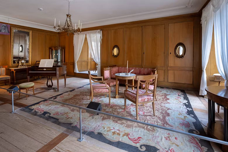 Ein Raum im Wohmuseum von Schloss Hallwyl mit Teppich, Klavier und weiteren Möbeln.