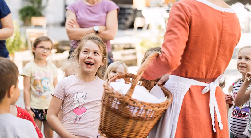 Eine Gruppe Kinder steht vor einer Magd, ein Mädchen lächelt freudig.