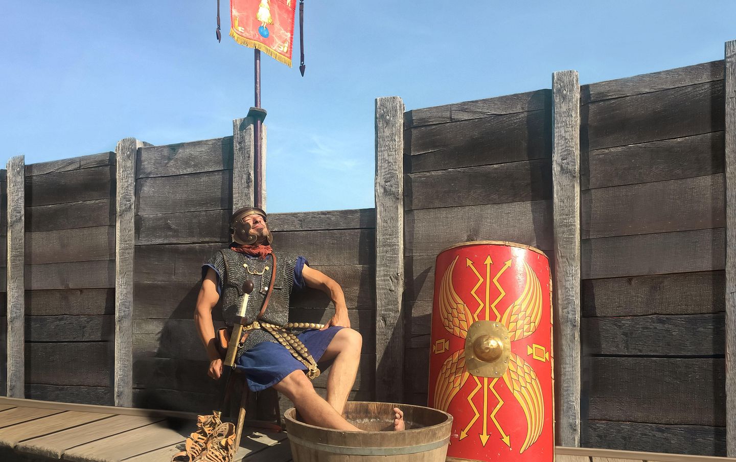 Ein Legionär sitzt auf einem Stuhl und blickt entspannt in die Sonne. Seine Füsse baden in einem Bottich mit Wasser.