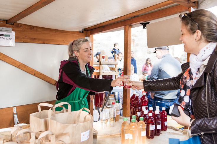 Marktfrau an den Mosttagen auf Schloss Hallwyl. Sie gibt einer Kundin etwas in die Hand.