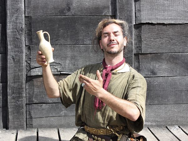 Ein als Römer gekleideter Mann hält eine kleine Amphore mit Garum im Legionärspfad Vindonissa.