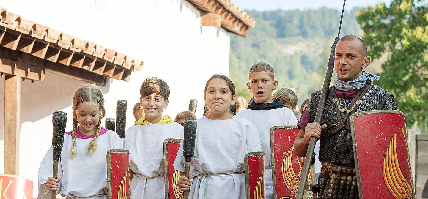 Ein Legionär marschiert mit einer Gruppe Mädchen und Buben nebeneinander wie die Römer.