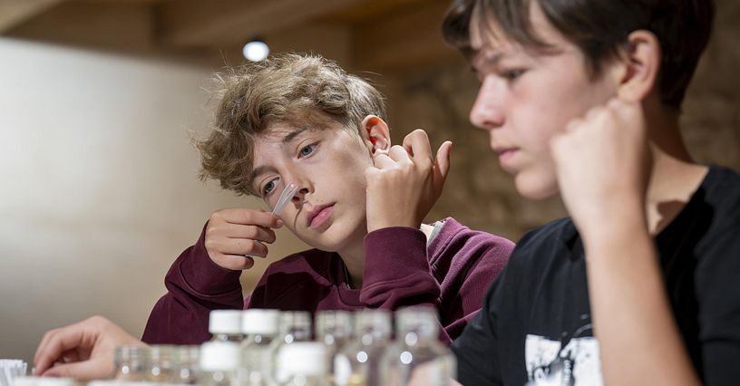 Ein junger Mann riecht an einem Riechstab, vor ihm steht eine Duftorgel mit verschiednenen Duftnoten