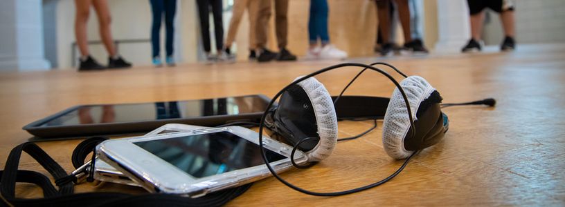 Audioguide-Gerät mit Kopfhörer, im Hintergrund in Unschärfe Schülerinnen und Schüler.