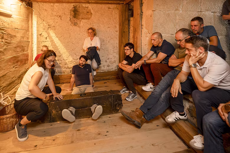 Eine Gruppe Männer und Frauen sitzen mit einer Museumsführerin im Gefängnis von Schloss Lenzburg. Eine Person liegt am Boden, die Füsse sind in einem Holz fixiert