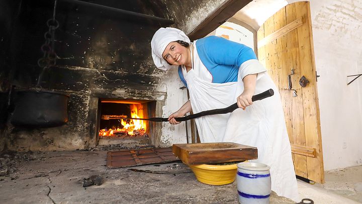 Eine als Köchin gekleidete Frau steht in der Schlossküche von Schloss Lenzburg und hantiert am Feuer.