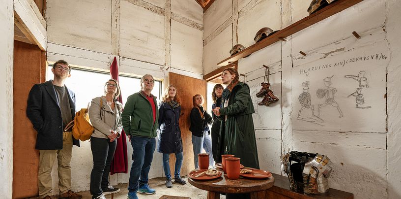 Eine Museumsführerin steht mit einer Gruppe in der Mannsschaftunterkunft Contubernia im Legionärspfad Vindonissa,