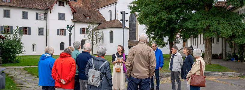 Eine Gästegruppe mit einer Museumsführerin steht vor der Kirche der Klosterhalbinsel Wettingen.