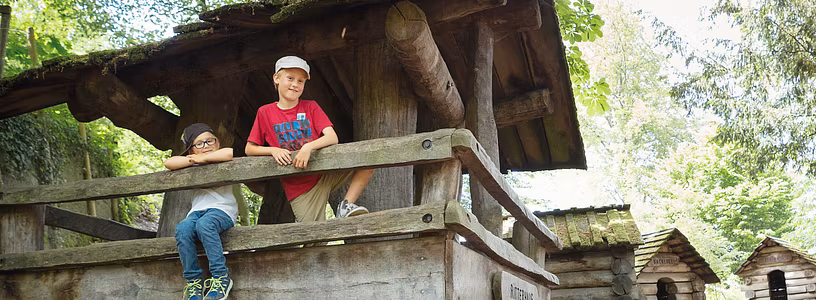 Spielplatz Schloss Lenzburg: Mehrere Holzhäuschen. Auf dem vordersten Häuschen stehen mehrere Kinder und blicken direkt in die Kamera.