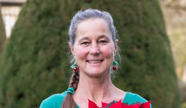Eine Frau steht vor Hecken und Bäumen im Garten von Schloss Wildegg. Sie lächelt in die Kamera und hält einen kleinen Weihnachtsstern.