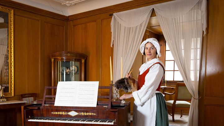Dienstmagd staubt Kerzenständer im Salon von Schloss Hallwyl ab