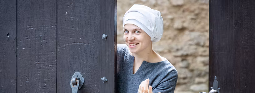 Eine mittelalterlich gekleidete Magd steht im Tor von Schloss Habsburg und winkt hinein..