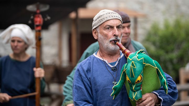 Ein mittelalterlich gekleideter Musiker mit einem Dudelsack in Form eines Drachens, im Hintergrund Mauern von Schloss Lenzburg.