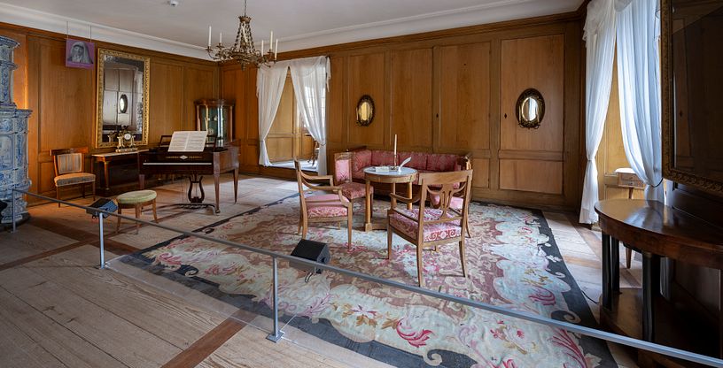 Ein Raum im Wohmuseum von Schloss Hallwyl mit Teppich, Klavier und weiteren Möbeln.