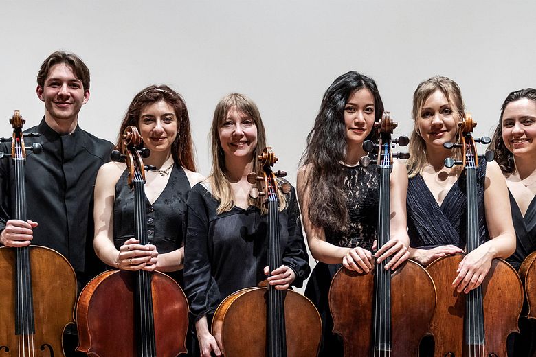 Gruppenbild: Acht Musikerinnen und Musiker mit ihren Celli stehen nebeneinander.