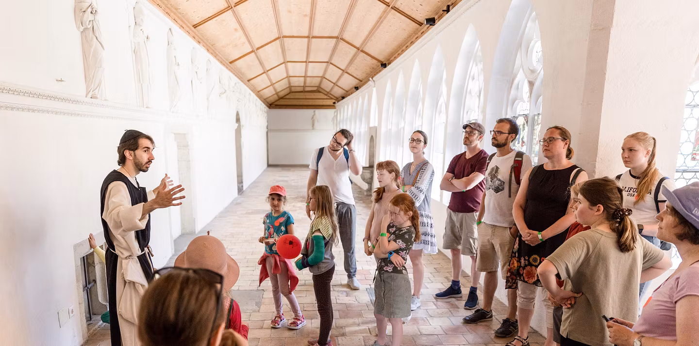 Ein Museumsführer im Kostüm eines Mönchs. Er steht im Kreuzgang des Klosters Wettingen vor einer Gruppe Besucherinnen und Besucher. 