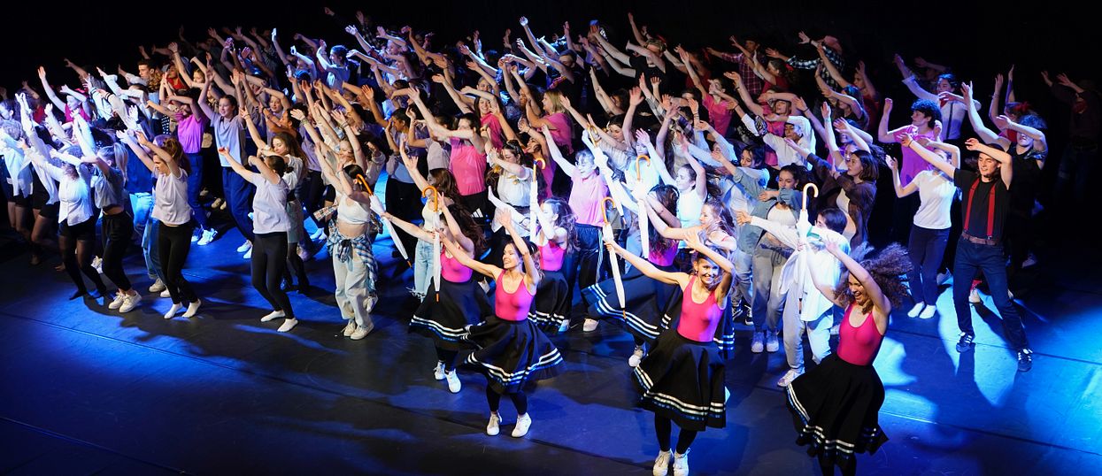 Viele Menschen tanzen zusammen auf einer Bühne. 