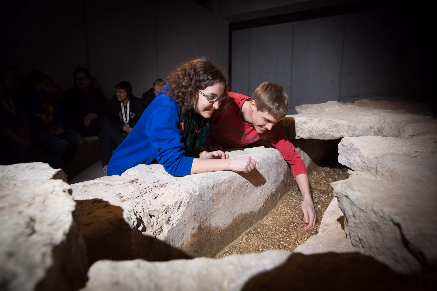 Zwei Personen beugen sich über Steine der Wasserleitung von Vindonissa und tauchen ihre Hände ins Wasser