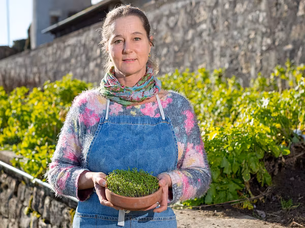 Eine Frau steht mit Gärtnerinnen-Kleidung im Garten.