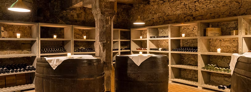 Weinkeller Schloss Habsburg. Gestelle mit Wein sowie grosse Weinfässer mit weischen Tischtüchern.