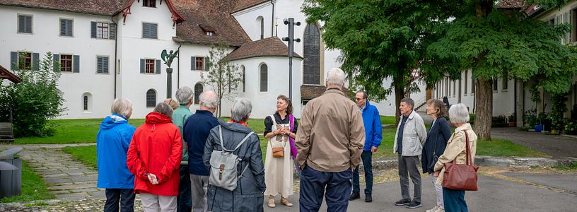 Eine Gästegruppe mit einer Museumsführerin steht vor der Kirche der Klosterhalbinsel Wettingen.
