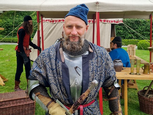Ein mittelalterlich gekleideter Mann in Rüstung blickt direkt in die Kamera