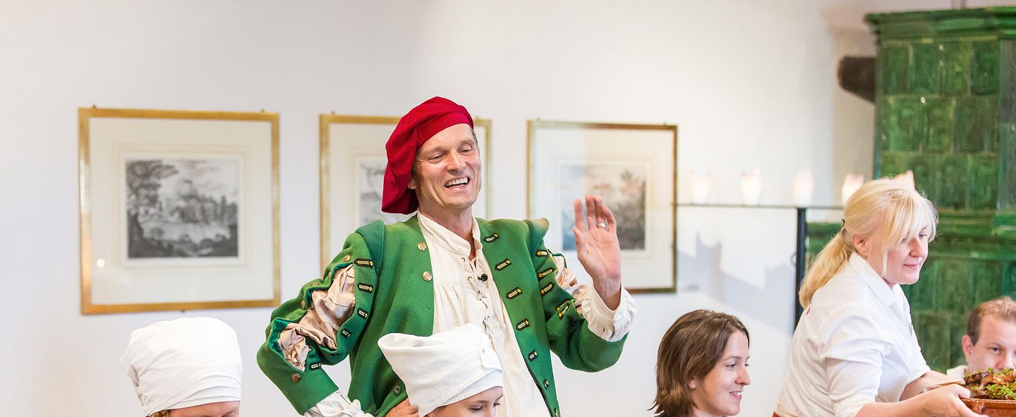 Ein Schauspieler im historischen Kostüm stehen in einem Restaurant. Um ihn herum essen Restaurantgäste auf Schloss Habsburg.
