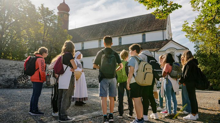 Eine Klostermagd steht mit einer Gruppe Schülerinnen und Schülern vor dem Kloster Wettingen.