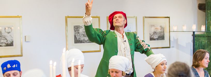 Verkleideter Museumsführer erzählt im Esstheater den dinierenden Gästen am Esstisch Anekdoten auf Schloss Habsburg