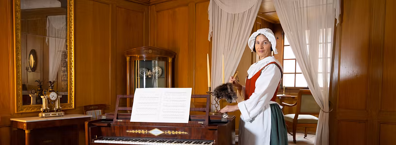 Eine mittelalterlich gekleidete Magd steht in einem eingerichteten Wohnzimmer im Museum von Schloss Hallwyl