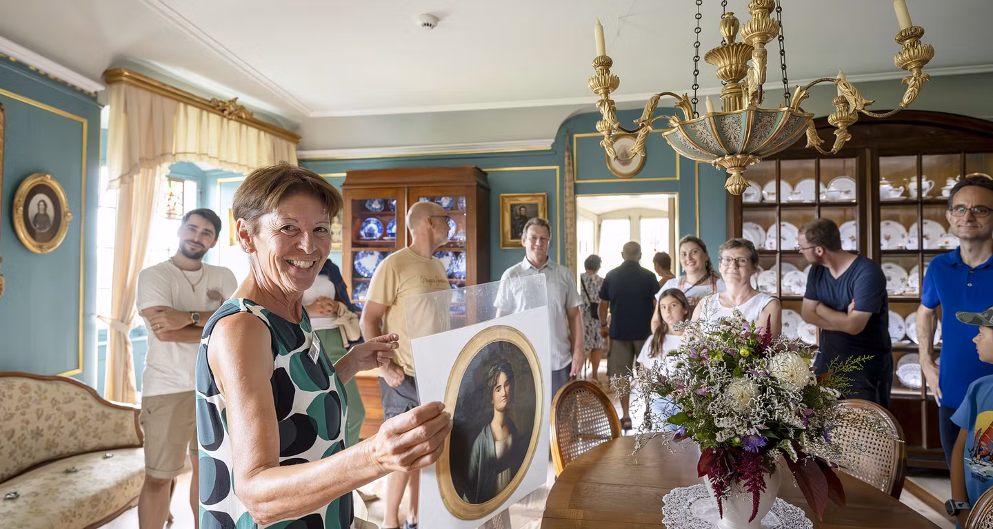 Eine Museumsführerin mit einer Gruppe Besucherinnen und Besucher in einem historischen Raum von Schloss Wildegg. Die Frau blickt direkt lachend in die Kamera.