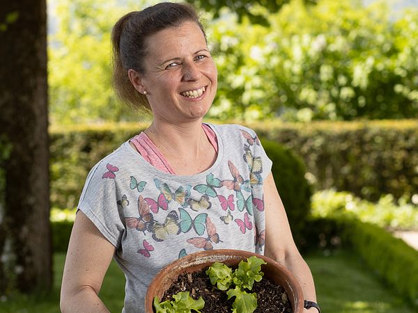 Porträt von Gärtnerin Melissa Gögele im Garten von Schloss Wildegg. Sie steht und hält einen Pflanzentopf mit beiden Händen.