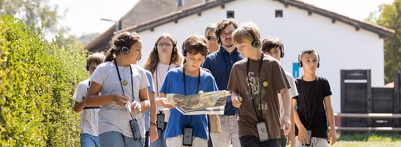 Eine Schulklasse unterwegs auf einem Kiesweg; im Hintergrund die rekonstruierte Unterkunft von Legionären.
