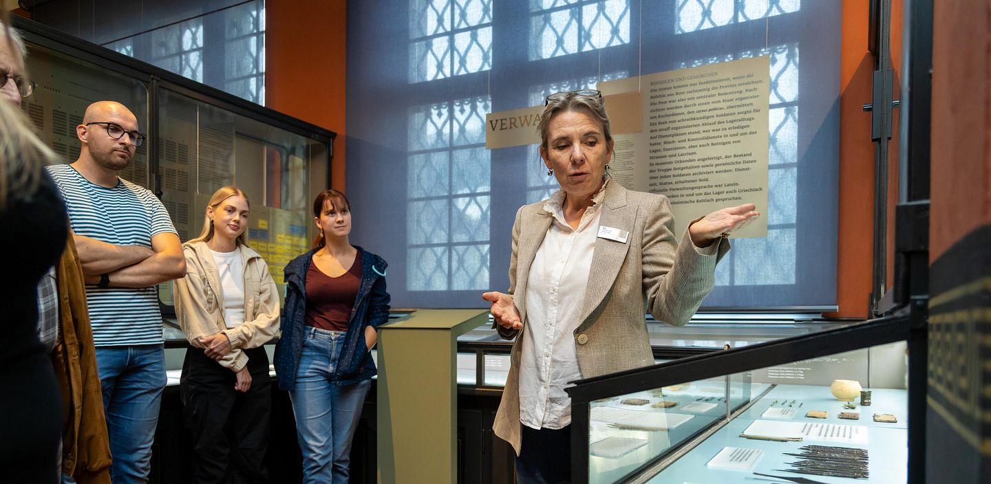 Eine Frau erklärt mehreren Besuchenden unterschiedliche Objekte in einer Vitrine im Vindonissa-Museum