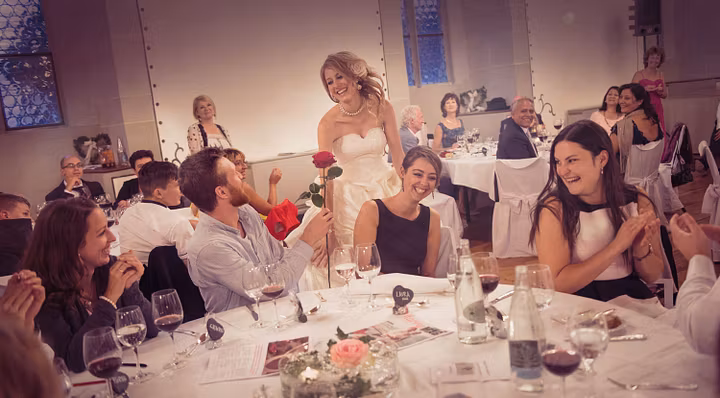 Hochzeit auf Schloss Lenzburg: Eine Braut steht an einem festlich gedeckten Tisch mit Gästen im Rittersaal von Schloss Lenzburg.