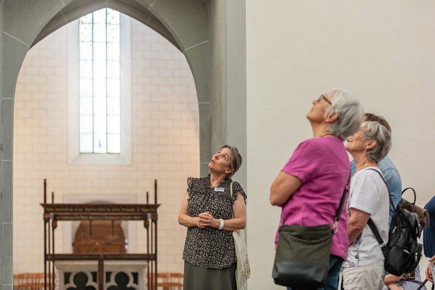 Eine Museumsführerin steht mit Besucherinnen im Kloster Königsfelden, im Hintergrund ein hohes Glasfester im Chor der Klosterkirche.