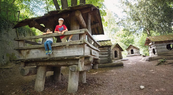 Spielplatz Schloss Lenzburg: Mehrere Holzhäuschen. Auf dem vordersten Häuschen stehen mehrere Kinder und blicken direkt in die Kamera.