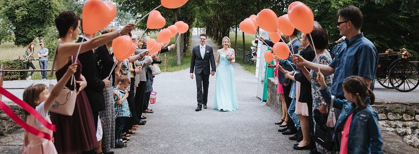 Ein Hochzeitspaar schreitet durch eine Festgesellschaft, die vor Schloss Hallwyl Spalier steht.