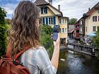 Eine Frau steht mit einem Handy in der Hand an einem Fluss.