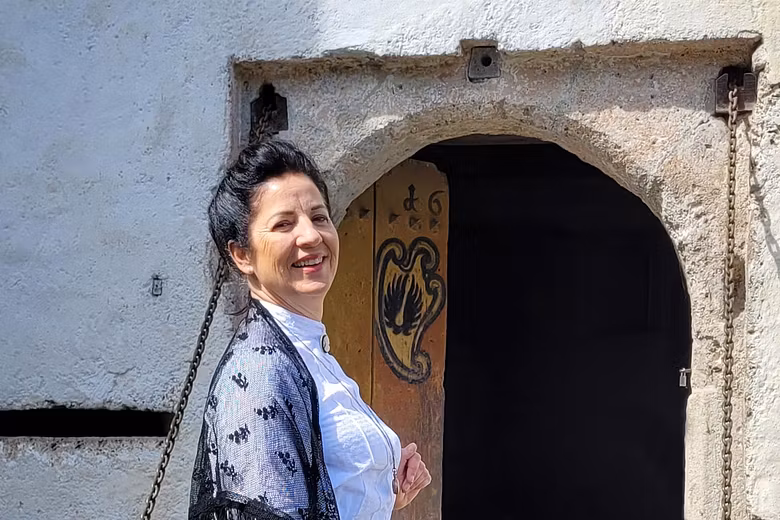 Eine Museumsführerin im historischen Kostüm vor einem Tor von Schloss Hallwyl. Sie blickt direkt in die Kamera und lacht.