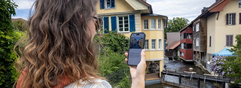 Eine Frau steht mit einem Handy in der Hand an einem Fluss.