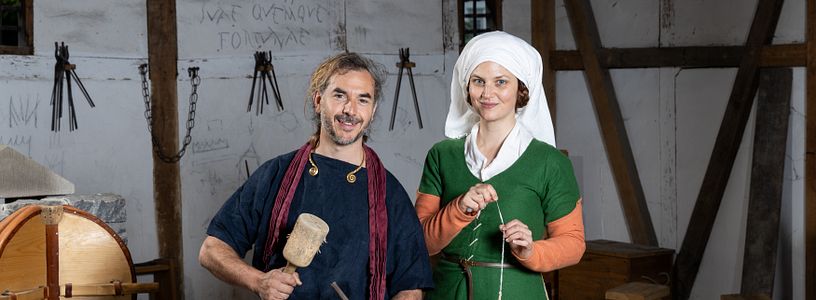 Ein römischer Steinmetz und eine mittelalterlich gekleidete Frau mit Wolle