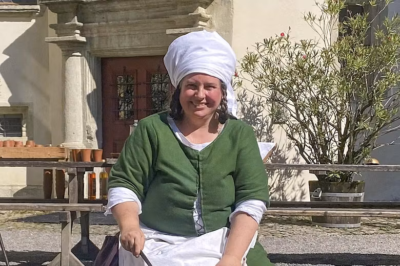 Eine mittelalterlich gekleidete Frau sitzt an einem Feuer im Hof von Schloss Lenzburg und kocht. 