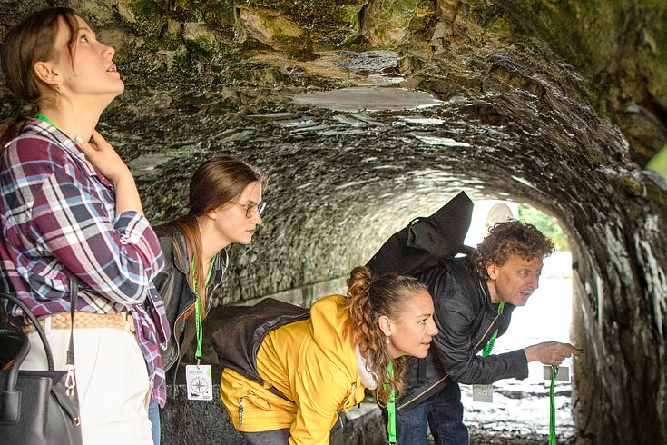Drei Frauen und ein Mann stehen in Freizeitkleidung in einer Höhle auf der Klosterhalbinsel Wettingen (Foxtrail). Sie blicken verwundert an die Wand rechts.