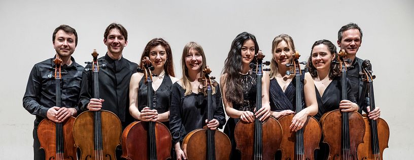 Gruppenbild: Acht Musikerinnen und Musiker mit ihren Celli stehen nebeneinander.