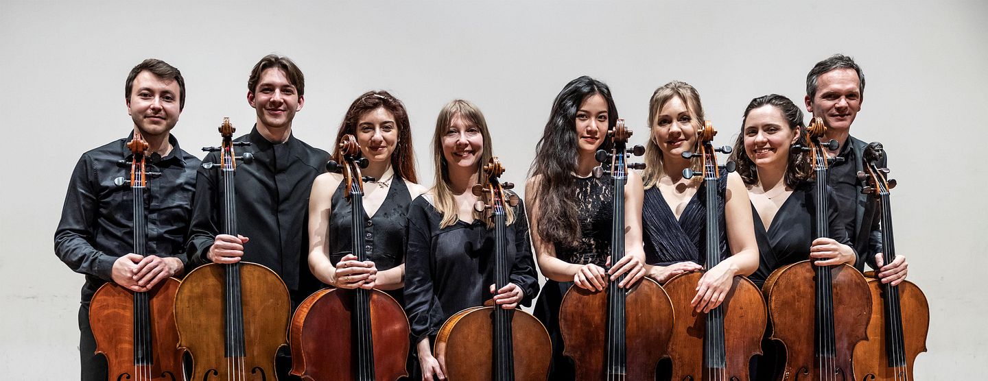 Gruppenbild: Acht Musikerinnen und Musiker mit ihren Celli stehen nebeneinander.