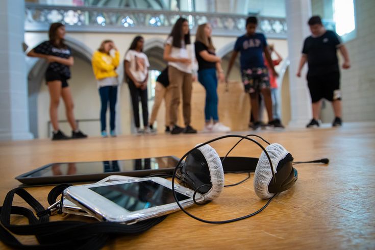 Audioguide-Gerät mit Kopfhörer, im Hintergrund in Unschärfe Schülerinnen und Schüler.