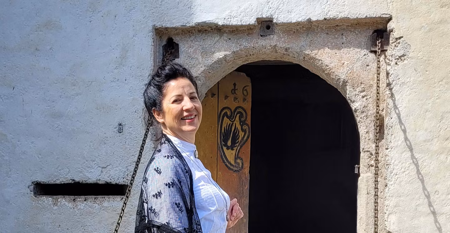 Eine Museumsführerin im historischen Kostüm vor einem Tor von Schloss Hallwyl. Sie blickt direkt in die Kamera und lacht.