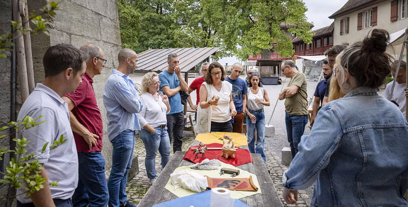 Eine Gruppe Männer und Frauen stehen im Hof von Schloss Lenzburg um einen Tisch. Auf diesem sind verschiedene Gegenstände platziert.